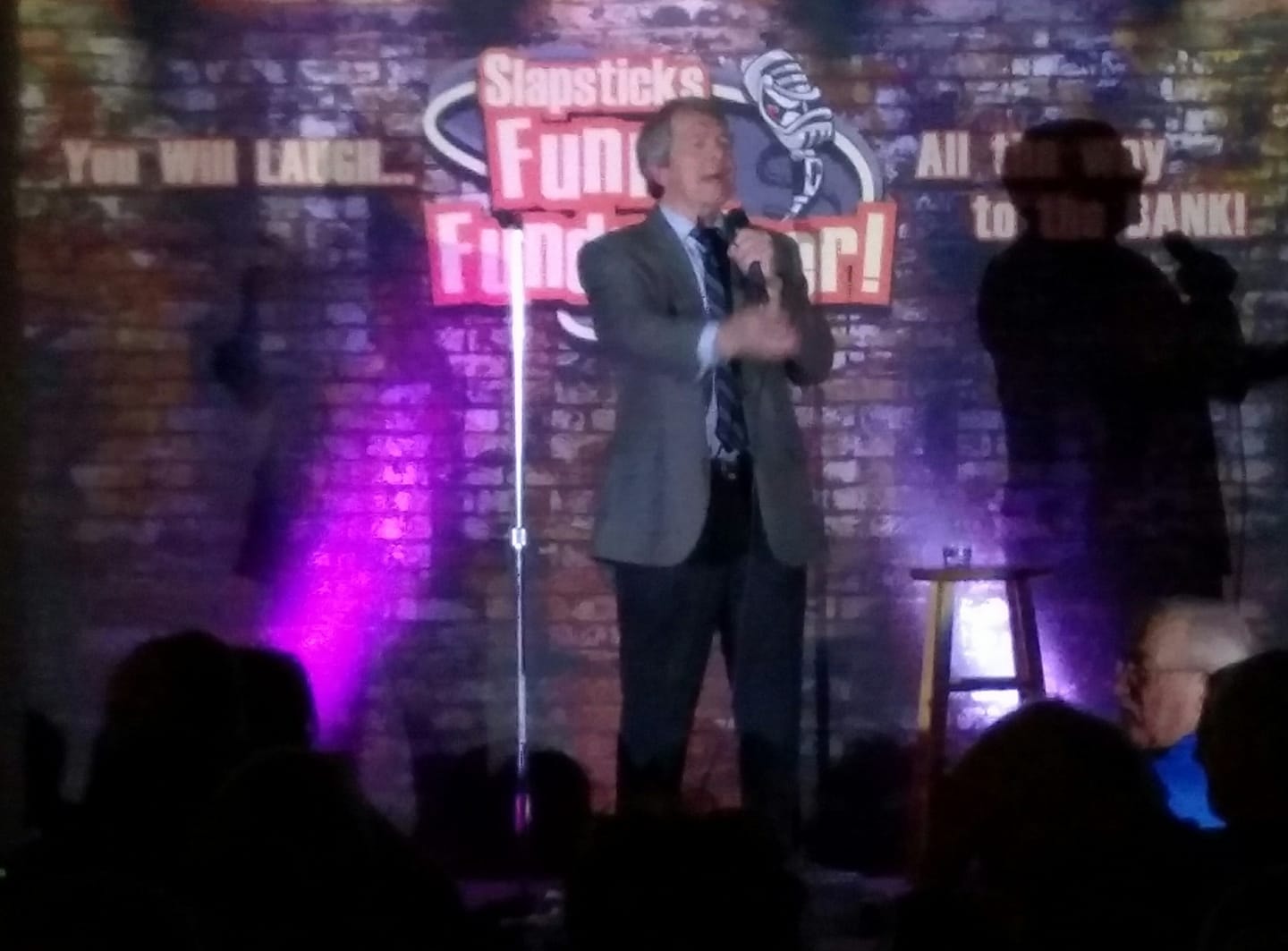 Dave Dugan performing on stage at Slapsticks Funny Fundraiser comedy event